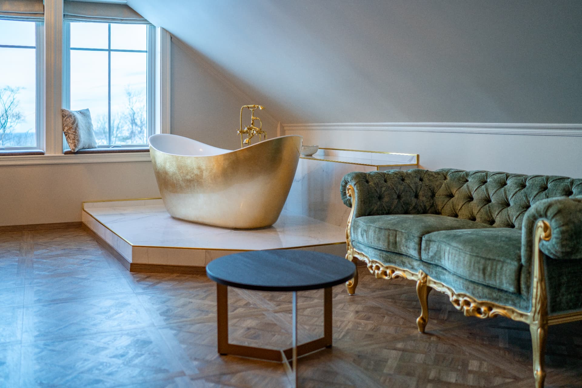 URE suite — gold slipper bath, green velvet sofa and parquet under the sloped ceiling