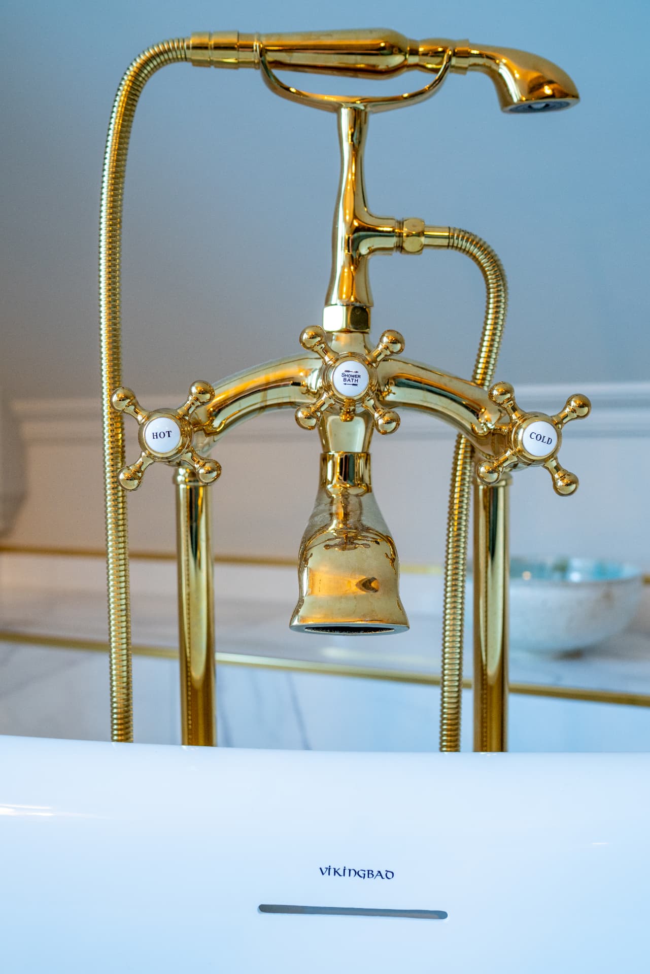 URE bathroom — polished brass bath fittings on a white freestanding tub