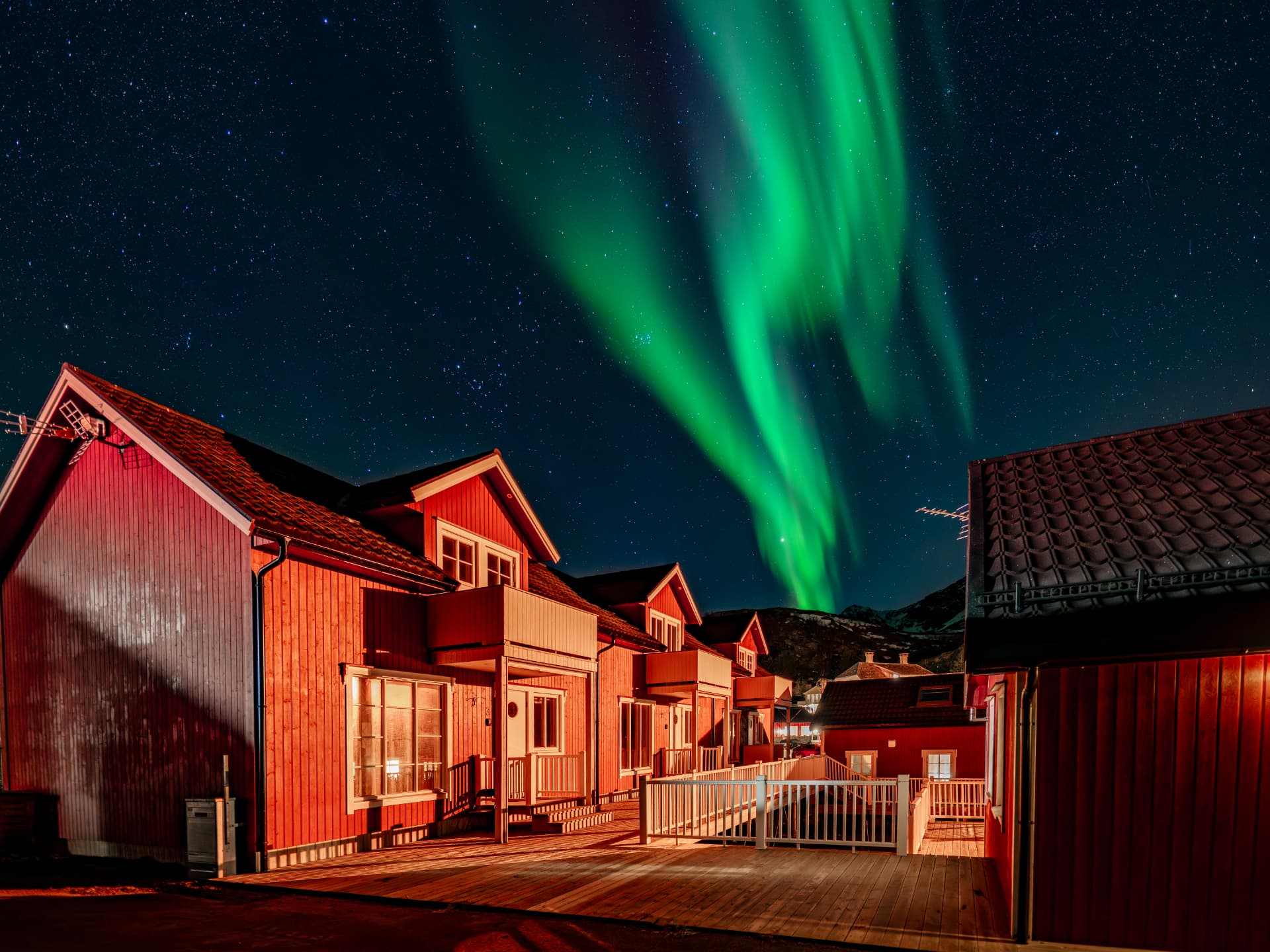 Green northern lights above the red buildings of URE Lodge